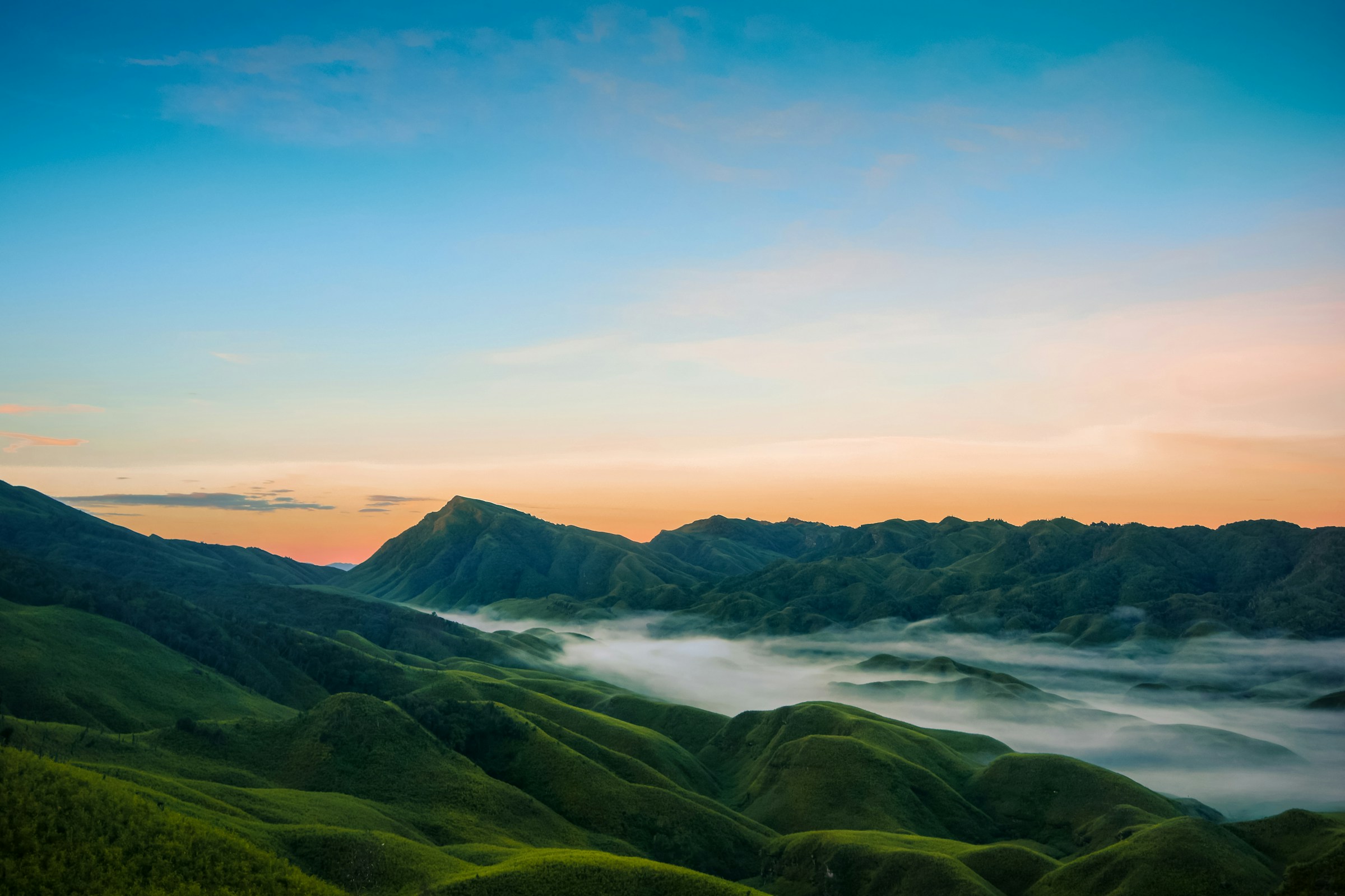 Green mountain ridges emerging from a sea of clouds at dawn