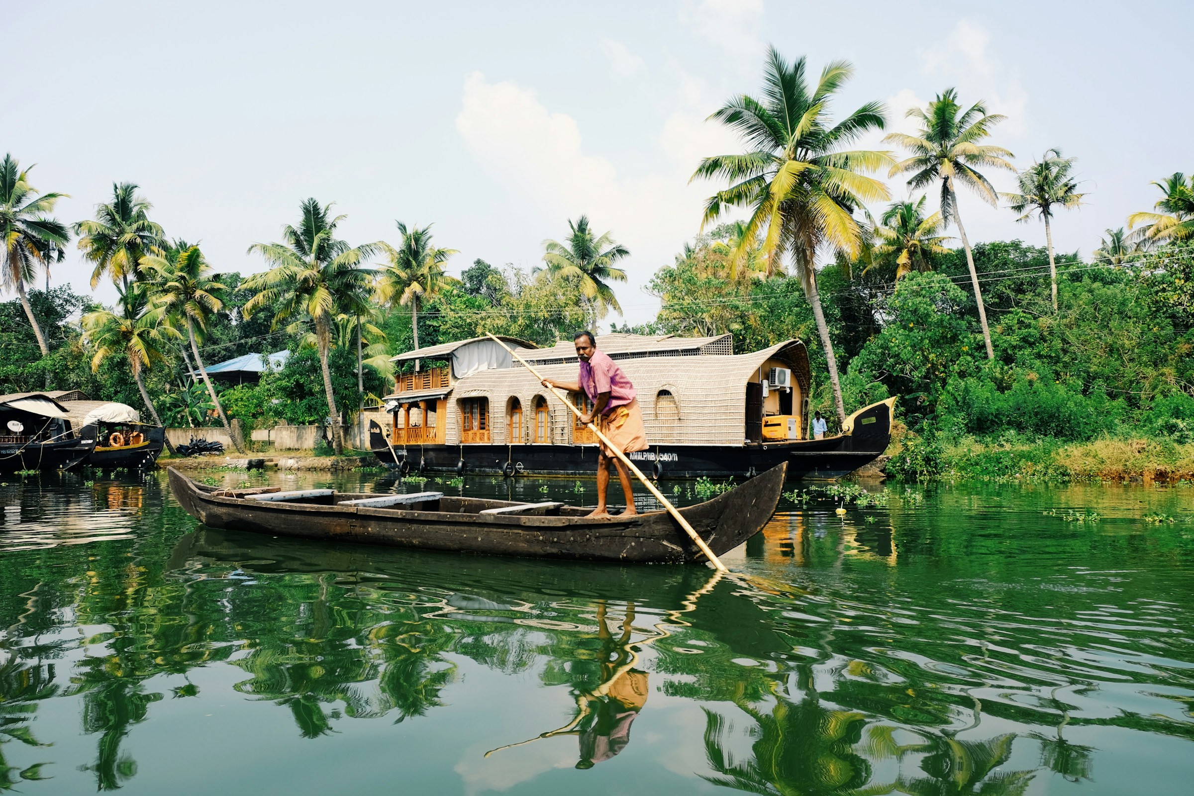 Traditional houseboats and a canoe on a green Kerala waterway
