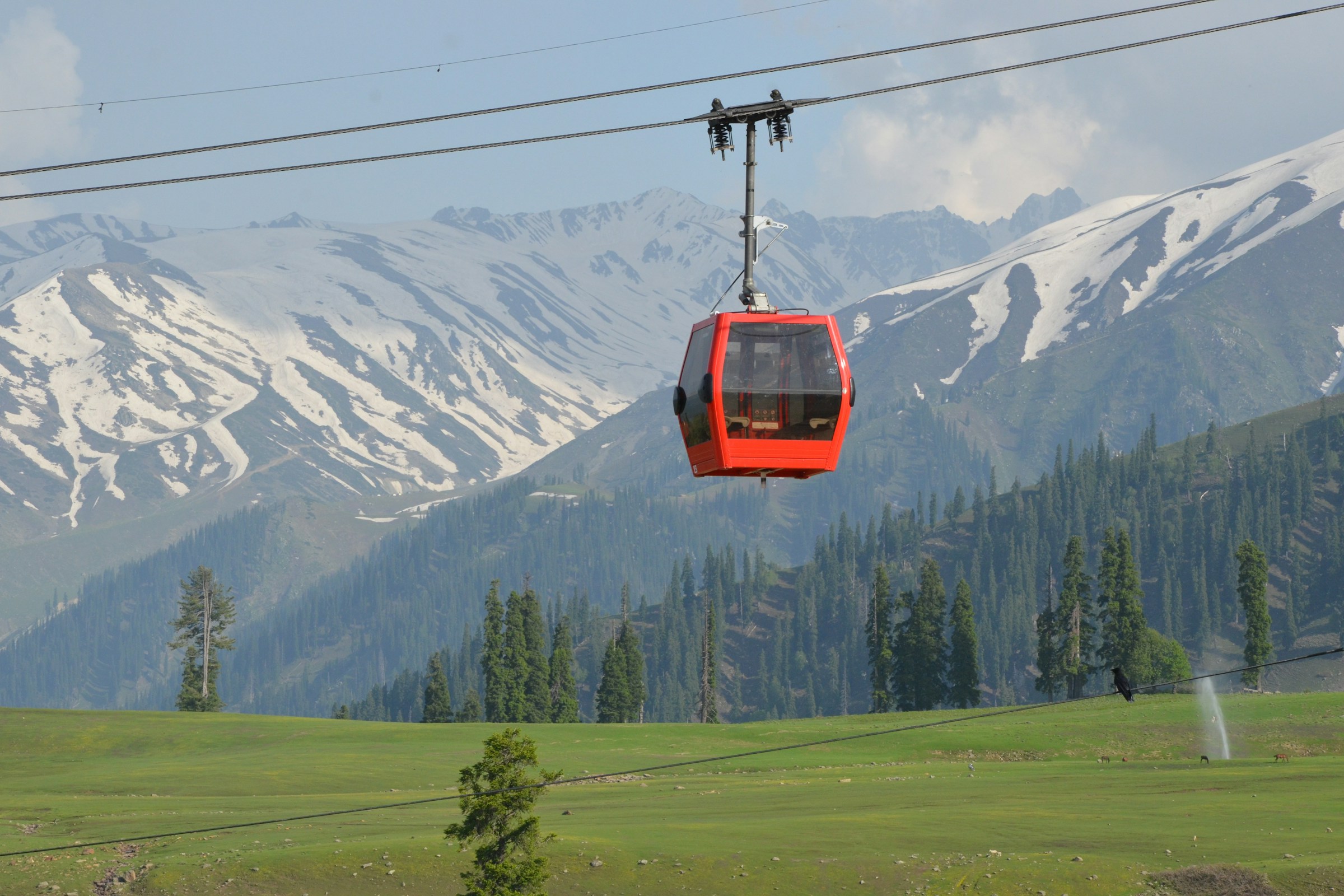 A red gondola above green slopes and snowy mountains