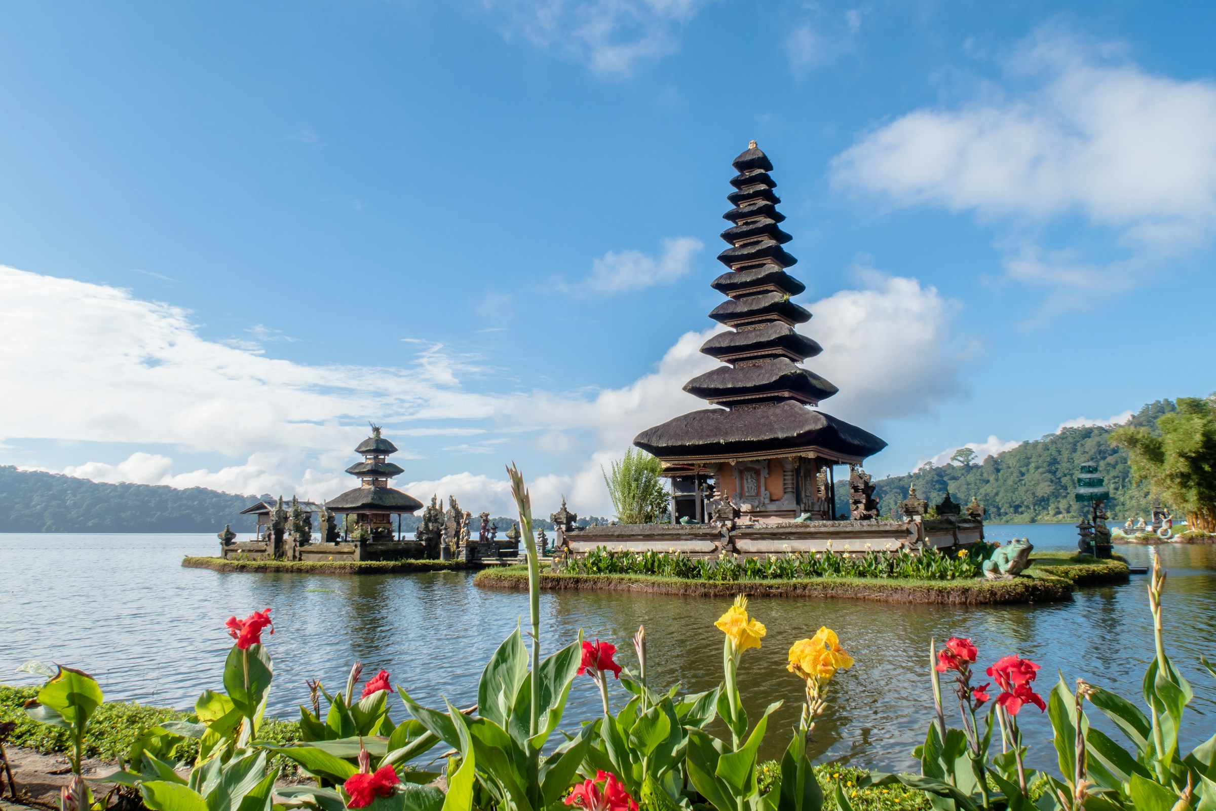 A Balinese temple beside a lake, framed by flowers and mountains