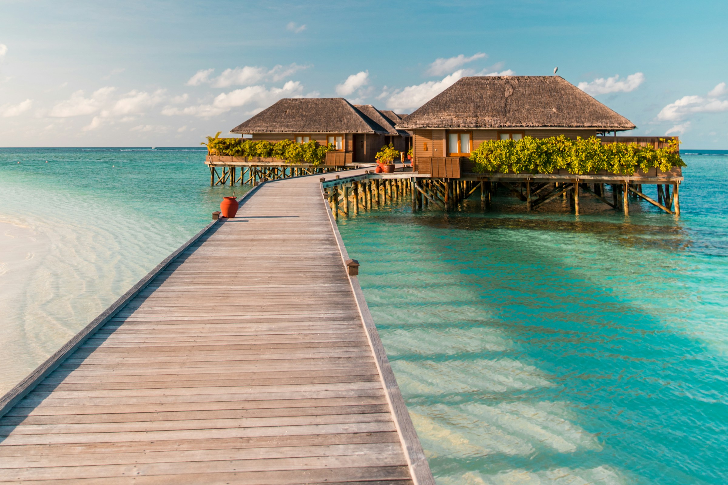 An overwater boardwalk leading to villas in a turquoise lagoon